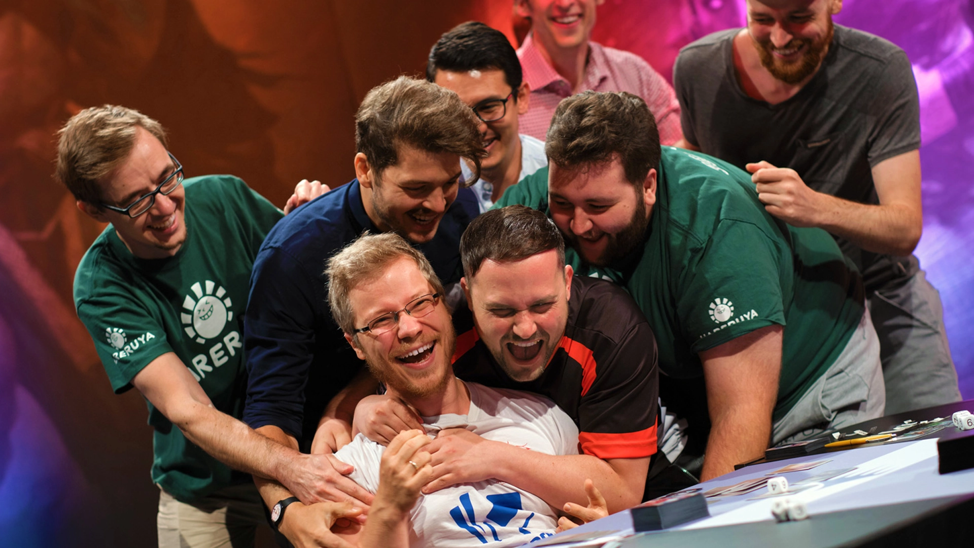 A group of players celebrate a victory at the Pro Tour. They pile onto the winner, all of them soaking up this momentous win